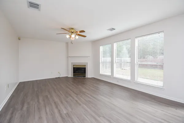 an empty room with wooden floor chandelier fan and windows