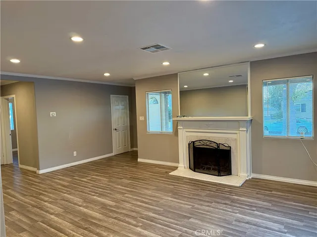 an empty room with wooden floor fireplace and windows