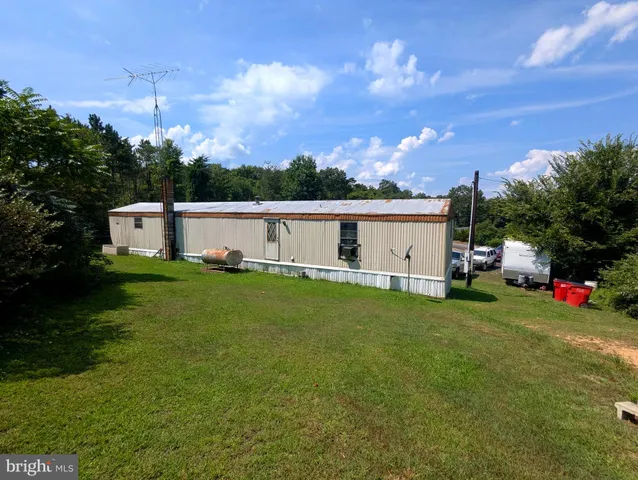 a view of a white house in front of a big yard with plants and large trees