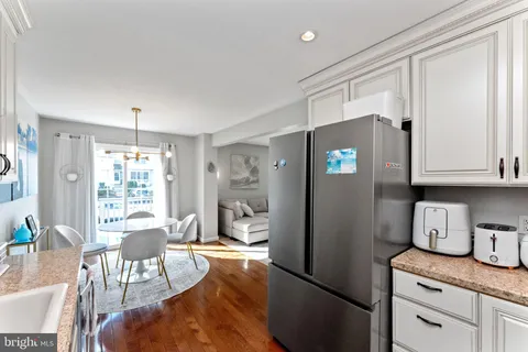 a kitchen with stainless steel appliances granite countertop a refrigerator a stove a sink dishwasher and white cabinets with wooden floor