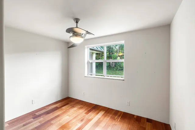 an empty room with wooden floor ceiling fan and windows