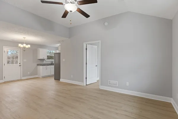 a view of an empty room with wooden floor and a kitchen