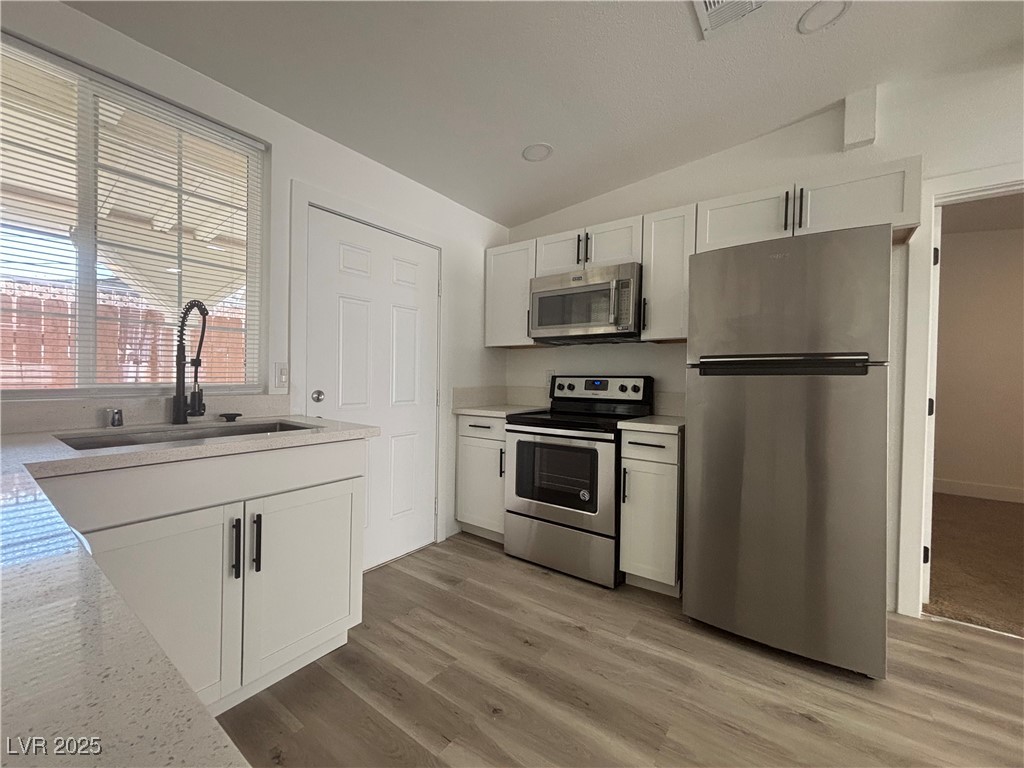 724 North 9th Street, Unit 2 Las Vegas, NV 89101 - Photo 1 of 10 Kitchen featuring appliances with stainless steel finishes, white cabinets, vaulted ceiling, light stone counters, and light wood finished floors