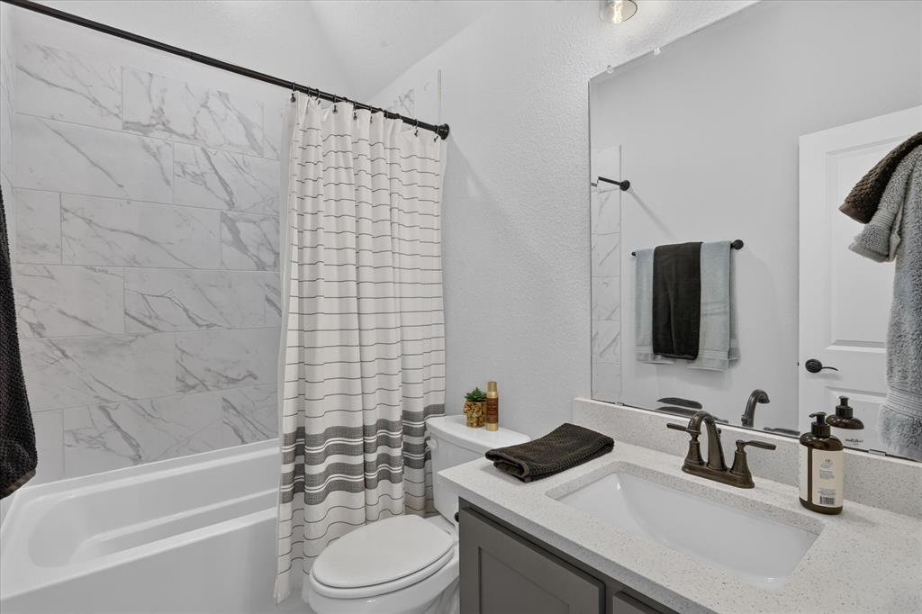 833 Godley Ranch Godley, TX 76044 - Photo 24 of 31 Bathroom featuring a white bathtub, large format marble-look tile surround, dark gray vanity with a light speckled countertop, undermount sink, and matte bronze fixtures