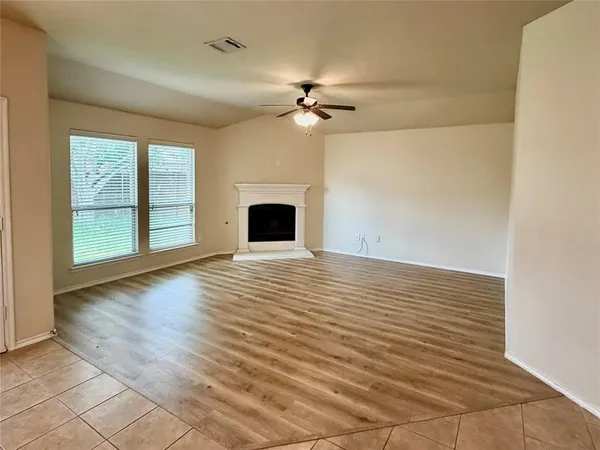 an empty room with wooden floor ceiling fan and windows
