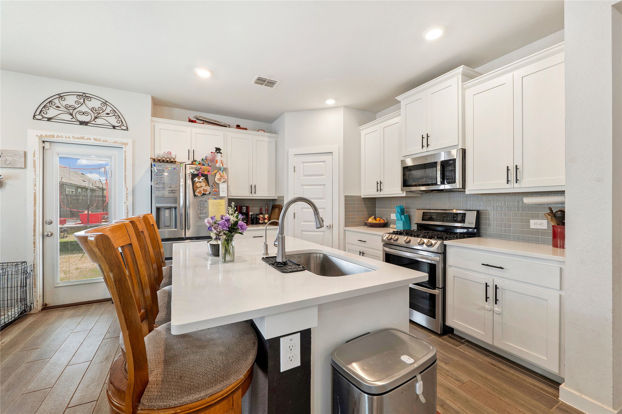 171 Acadia Drive Kyle, TX 78640 - Photo 7 of 26 Kitchen featuring stainless steel appliances, white cabinetry, wood finished flooring, an island with sink, and a kitchen bar