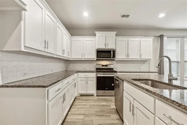 a kitchen with granite countertop white cabinets and stainless steel appliances