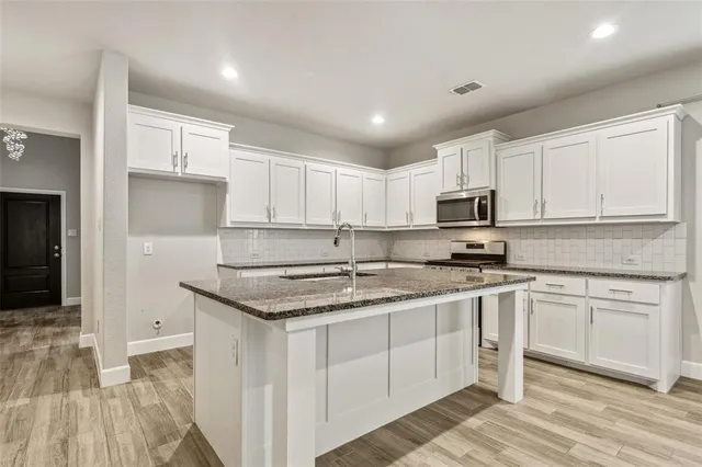 a kitchen with stainless steel appliances granite countertop a stove a sink and white cabinets