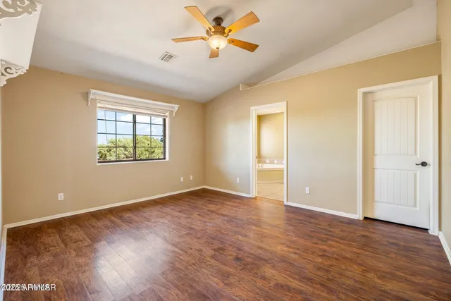 an empty room with wooden floor ceiling fan and windows