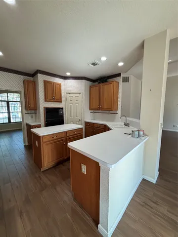 a large kitchen with stainless steel appliances a sink a stove top oven a wooden floor and cabinets