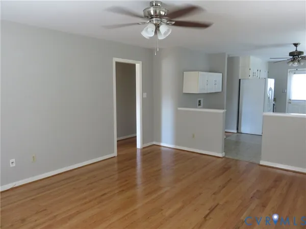 a view of an empty room with wooden floor and a ceiling fan
