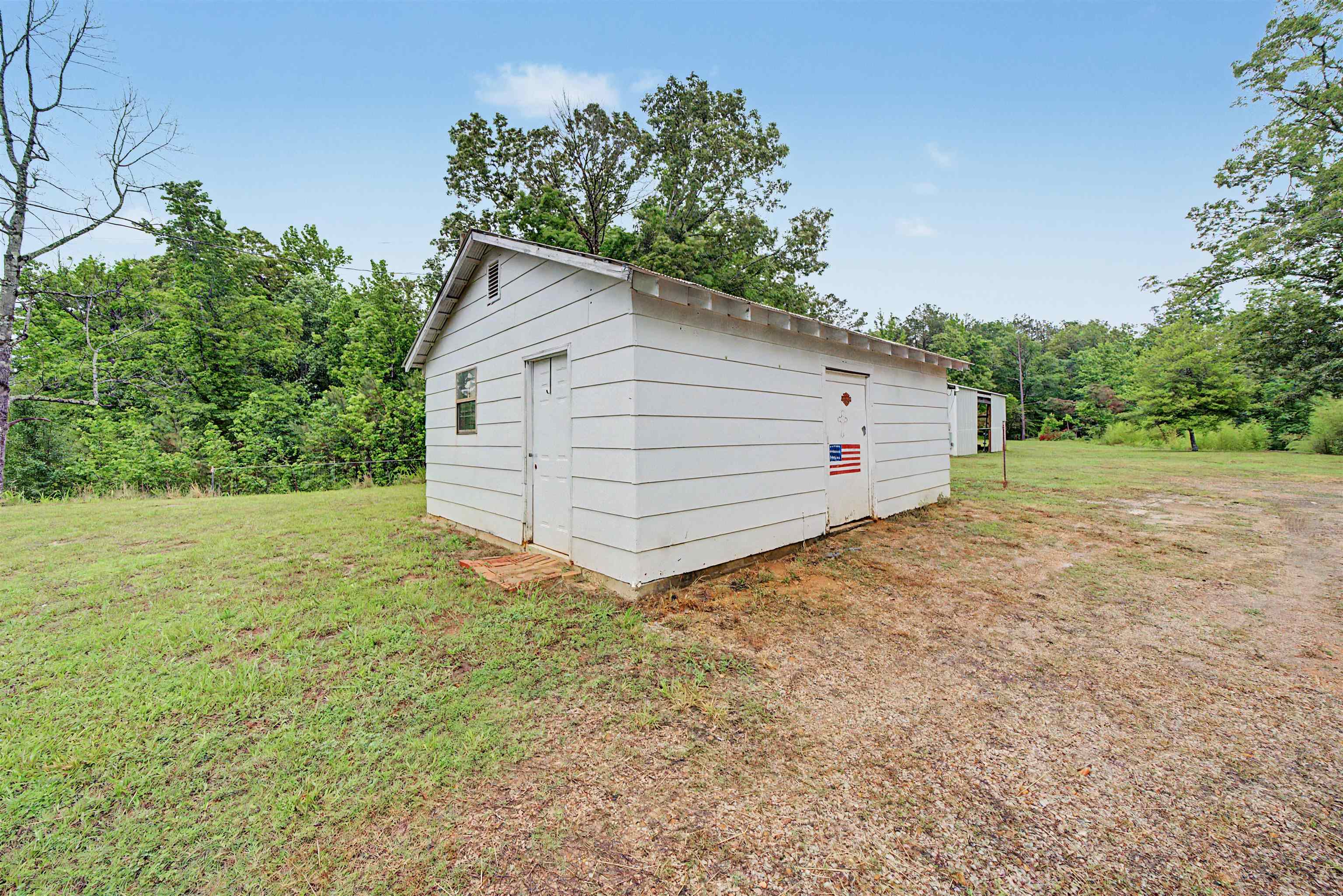6264 45th Highway South Ramer, TN 38367 - Photo 5 of 24 White-sided outbuilding with multiple entry doors and a gabled roofline, set on a gravel and grass lot
