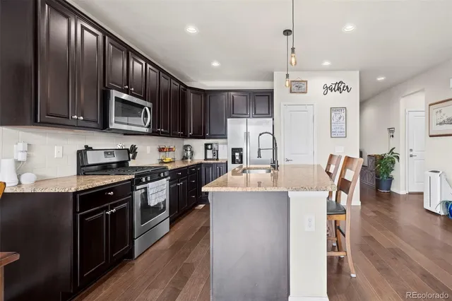 a open kitchen with stainless steel appliances granite countertop a stove top oven a sink dishwasher a dining table and chairs with wooden floor