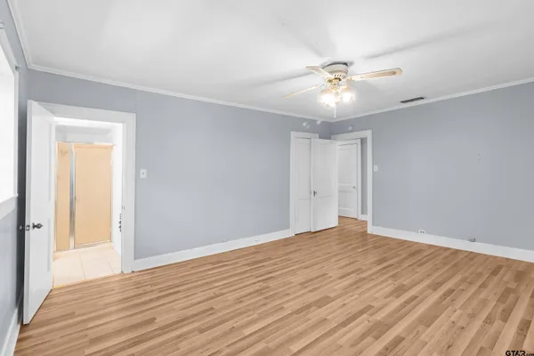 a view of an empty room with wooden floor and a ceiling fan