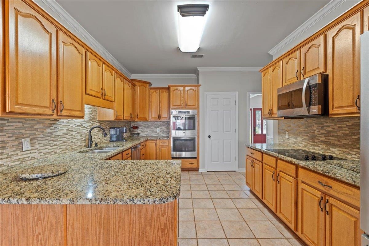 1675 John Ridge Drive Collierville, TN 38017 - Photo 16 of 39 Kitchen with appliances with stainless steel finishes, a sink, light stone countertops, tasteful backsplash, and crown molding
