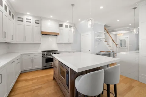 a kitchen with a stove a sink a kitchen island with chairs and wooden floor