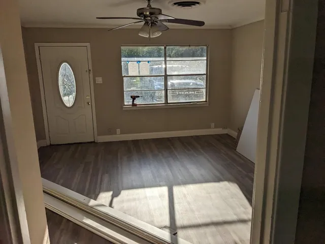 an empty room with wooden floor fan and windows