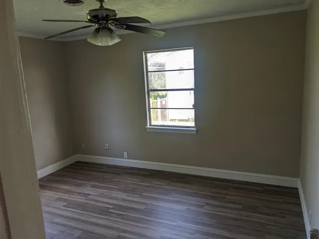 an empty room with wooden floor fan and windows