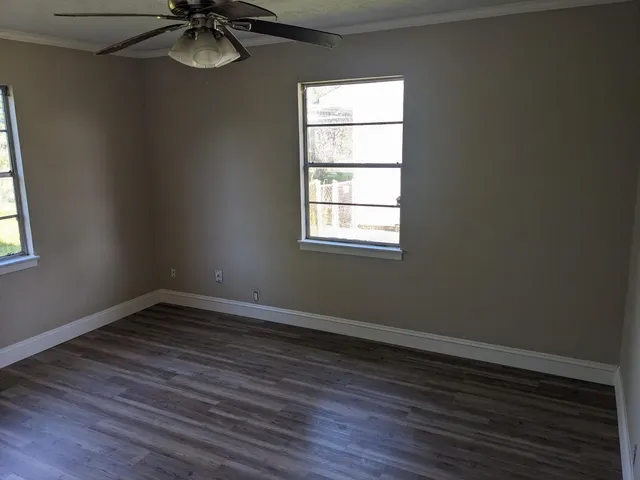 an empty room with wooden floor fan and windows