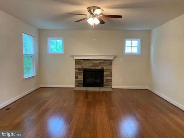 a view of an empty room with wooden floor fireplace and a window