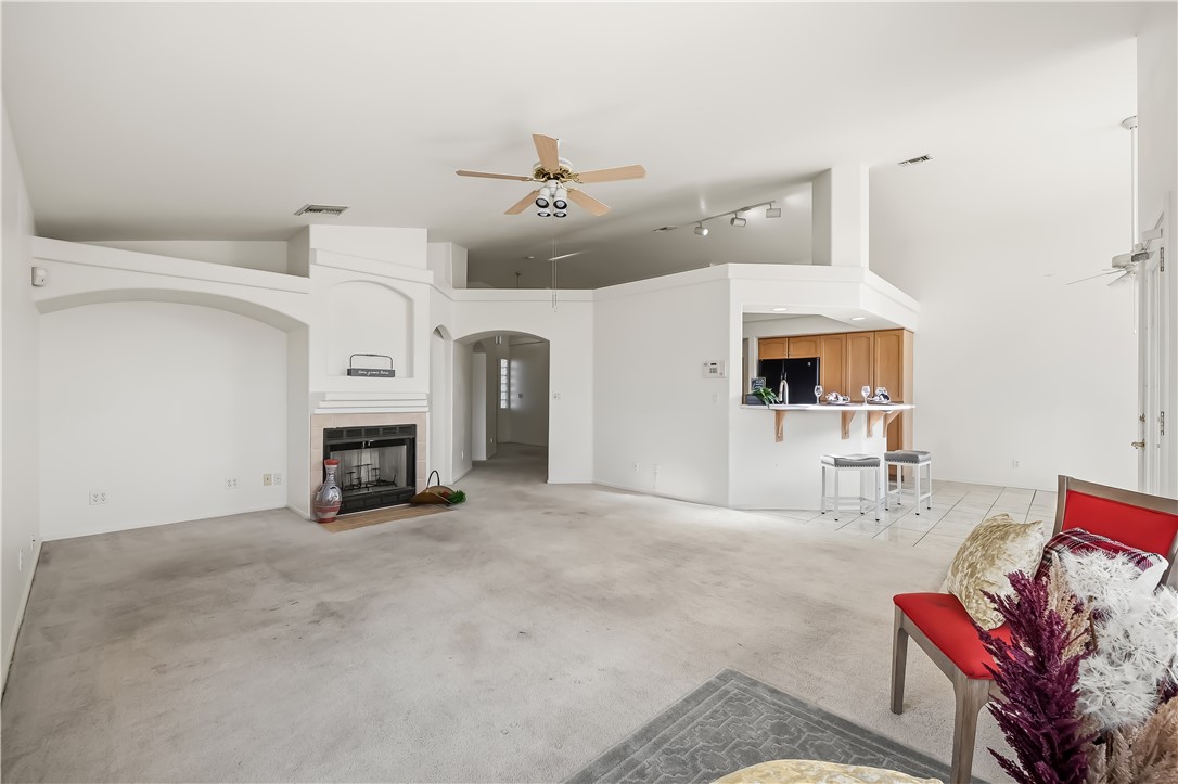 2853 Winchester Road Bullhead City, AZ 86442 - Photo 14 of 40 Spacious living area featuring a fireplace with a tiled surround, high ceilings, arched architectural details, a ceiling fan, and an open breakfast bar with wood-finish cabinetry