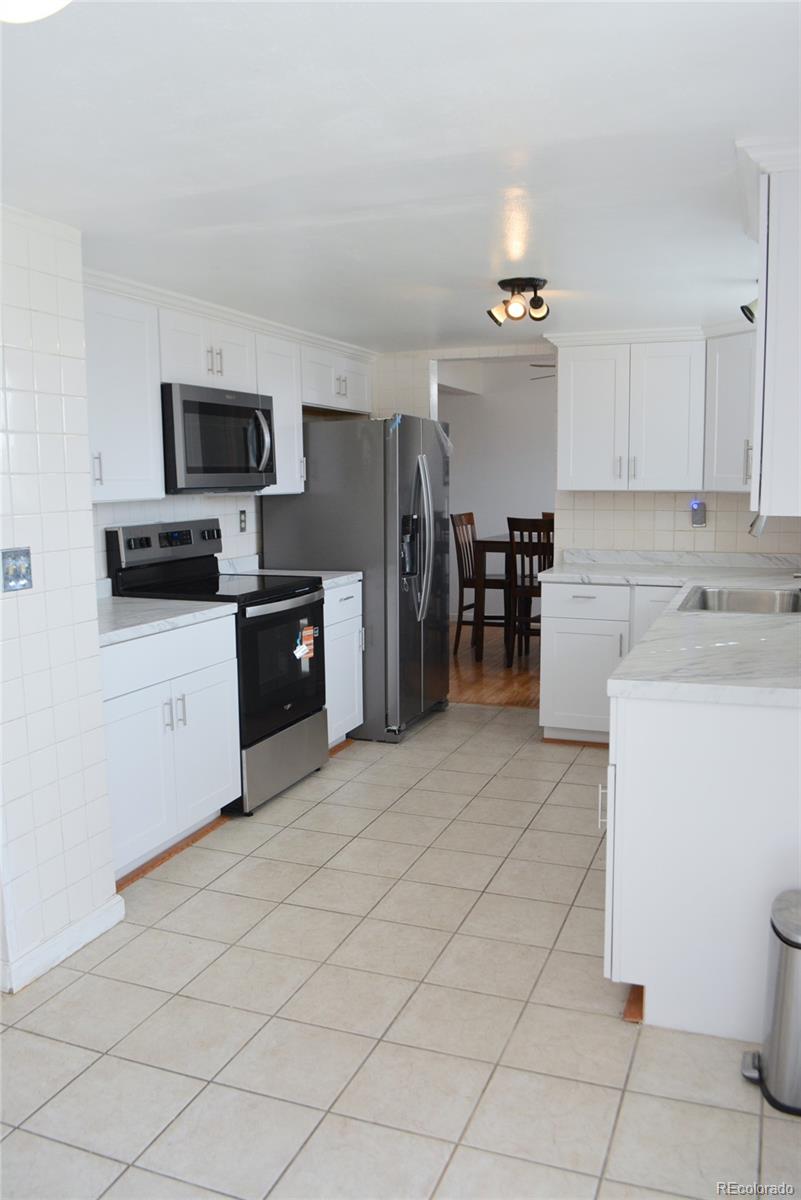 2087 South Quintero Street Aurora, CO 80013 - Photo 5 of 34 a kitchen with stainless steel appliances kitchen island granite countertop a refrigerator sink and white cabinets