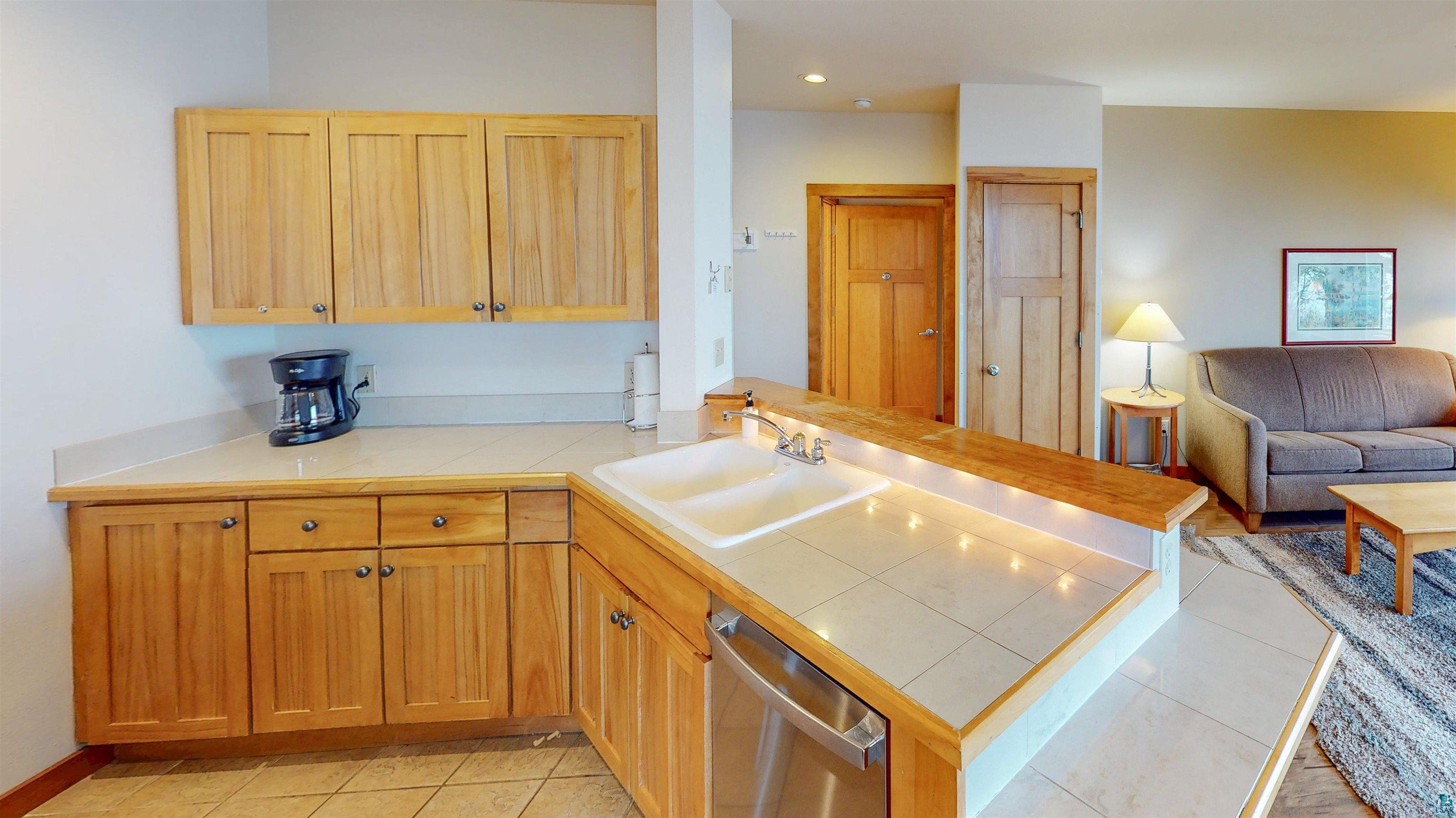 504-506 Poplar River Road, Unit 505 Lutsen, MN 55612 - Photo 7 of 39 Kitchen area featuring natural wood cabinetry, light-toned tile countertops, and a double basin sink with an integrated dishwasher