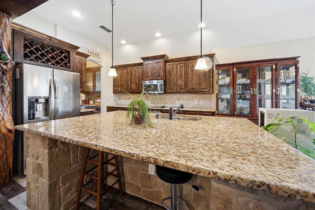 119 George Owens Road Ponder, TX 76259 - Photo 7 of 26 Kitchen featuring a large stone-wrapped island with a granite countertop, stainless steel appliances, dark wood cabinetry, and recessed lighting