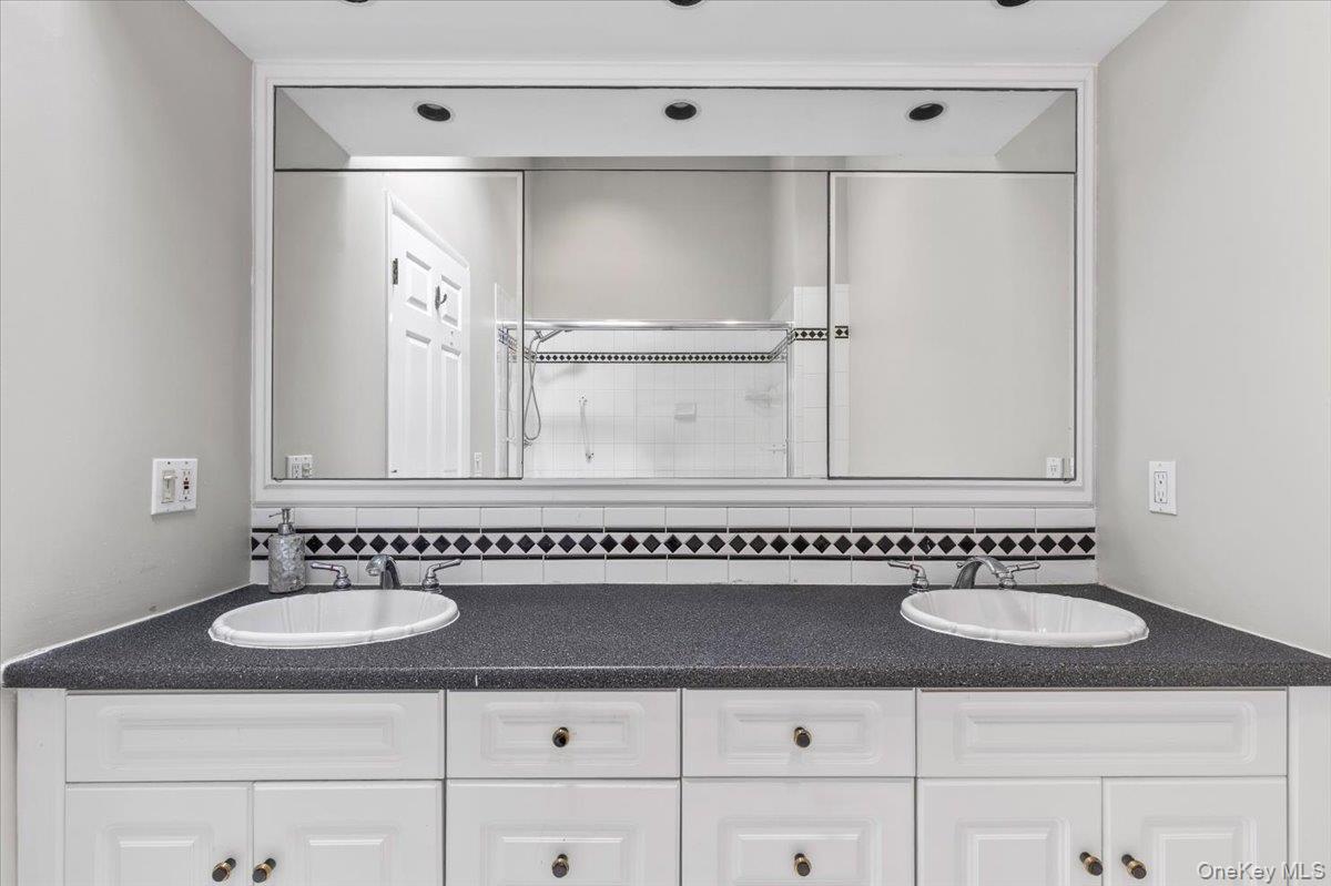 37 Talcott Road Rye Brook, NY 10573 - Photo 13 of 25 Dual vanity with white cabinetry, black speckled countertop, and integrated white oval sinks