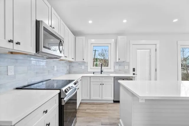 a view of kitchen island with stainless steel appliances granite countertop a sink dishwasher and wooden floor