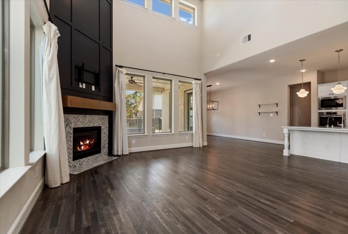 155 Rockwell Park Spring, TX 77389 - Photo 15 of 50 This photo showcases a spacious, open-concept living area with high ceilings and abundant natural light. It features a modern fireplace with a sleek mantel, large windows, and elegant dark wood flooring. The adjacent kitchen area includes a breakfast bar and contemporary lighting fixtures, creating an inviting space for entertaining.