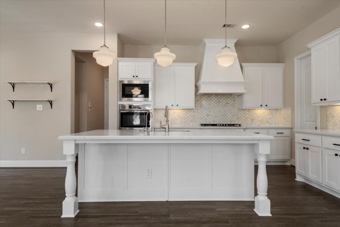 155 Rockwell Park Spring, TX 77389 - Photo 16 of 50 This kitchen features a spacious island with elegant pendant lighting, white cabinetry, and a mosaic tile backsplash. It includes modern stainless steel appliances, a stylish range hood, and dark wood flooring, offering a clean and inviting atmosphere.