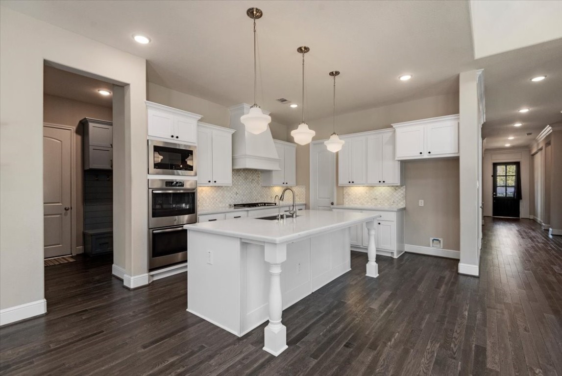 155 Rockwell Park Spring, TX 77389 - Photo 17 of 50 This kitchen features a spacious layout with a large island, modern stainless steel appliances, and elegant pendant lighting. The white cabinetry and dark wood flooring create a stylish contrast, enhanced by a tile backsplash.