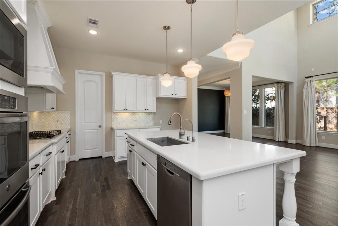 155 Rockwell Park Spring, TX 77389 - Photo 18 of 50 This spacious kitchen features modern white cabinetry, a large island with a sink, stainless steel appliances, and elegant pendant lighting. It opens to a bright living area with large windows and dark wood flooring, creating a welcoming and functional space.