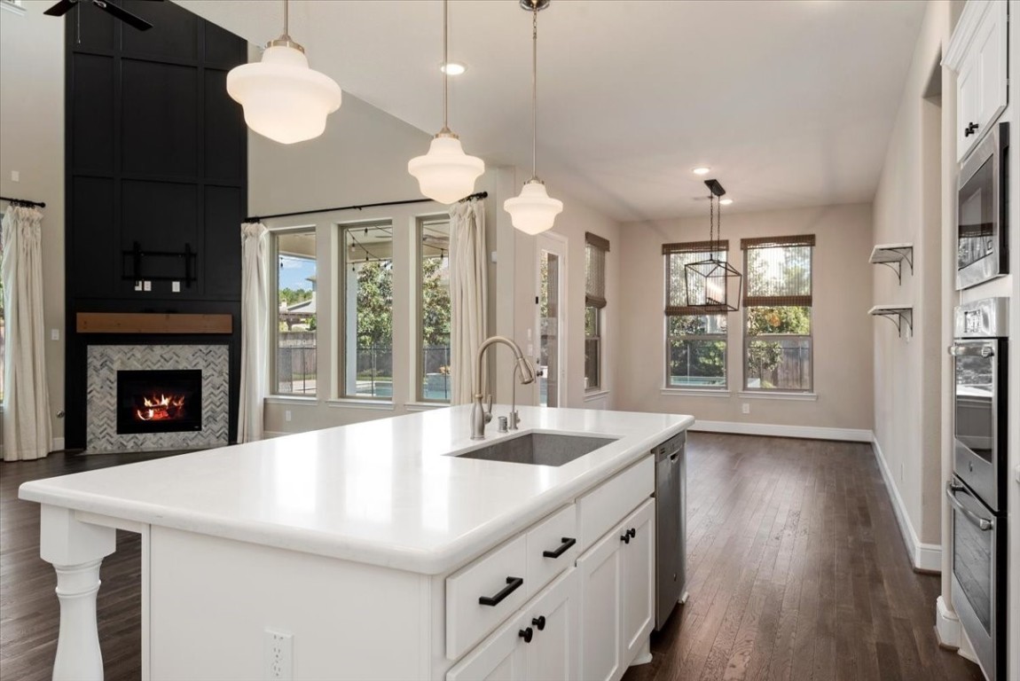 155 Rockwell Park Spring, TX 77389 - Photo 19 of 50 This photo showcases a modern, open-concept kitchen and living area. It features a large island with a sink, pendant lighting, and white cabinetry. The room has hardwood floors, a cozy fireplace with a stylish herringbone pattern, and ample natural light from multiple windows.