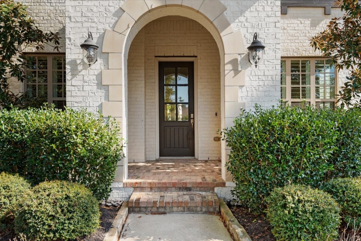 155 Rockwell Park Spring, TX 77389 - Photo 2 of 50 Charming entryway with a brick arch and dark wooden door, flanked by elegant lantern-style lights. The front is framed by manicured shrubs, giving a welcoming and sophisticated feel.