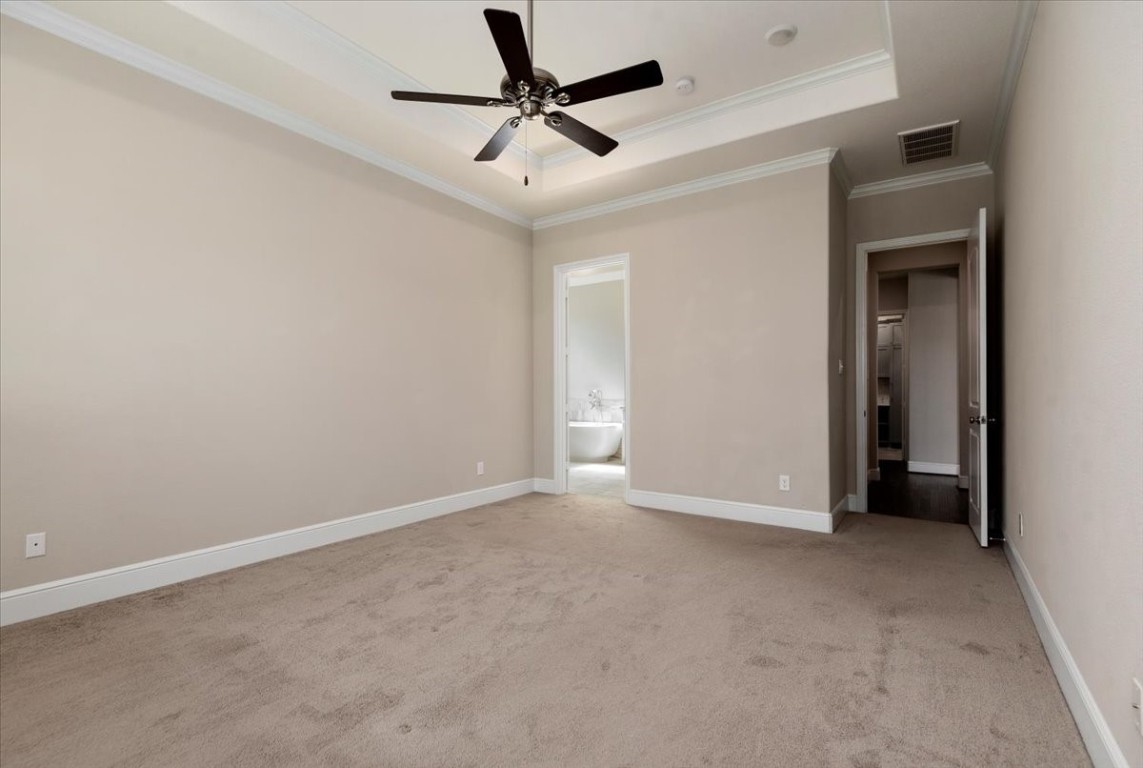 155 Rockwell Park Spring, TX 77389 - Photo 25 of 50 Spacious bedroom with neutral walls and carpet, featuring a ceiling fan. It connects to a bathroom with a glimpse of a freestanding tub, enhancing the suite's appeal.