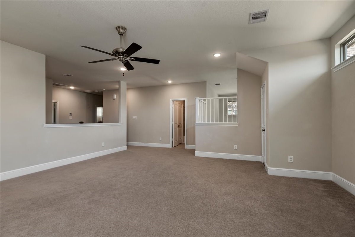 155 Rockwell Park Spring, TX 77389 - Photo 39 of 50 This spacious living area features neutral walls and carpeting, a ceiling fan, and recessed lighting. The room offers an open layout with a partial wall and railing, enhancing the airy feel.