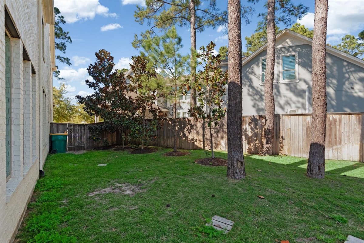 155 Rockwell Park Spring, TX 77389 - Photo 41 of 50 This photo showcases a side yard with a grassy area bordered by a wooden fence. Tall trees provide shade, and the space is adjacent to a light-colored brick house. Ideal for outdoor activities or gardening.
