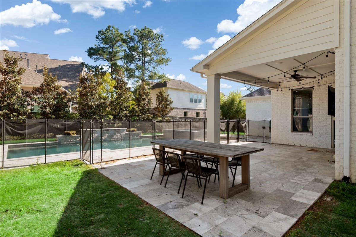 155 Rockwell Park Spring, TX 77389 - Photo 42 of 50 This backyard features a spacious patio with a wooden table and chairs, a covered area with a ceiling fan and string lights, and a fenced-in pool, offering a perfect blend of relaxation and entertainment space.