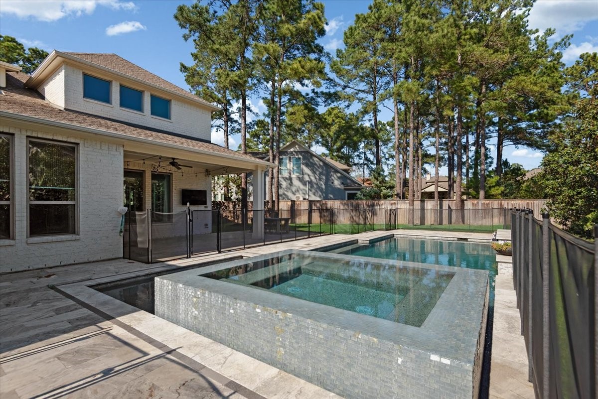155 Rockwell Park Spring, TX 77389 - Photo 47 of 50 This photo showcases a modern home with a spacious backyard that includes a luxurious pool and spa. The area is surrounded by tall trees, offering privacy and a serene atmosphere. The covered patio is perfect for outdoor relaxation and entertainment.