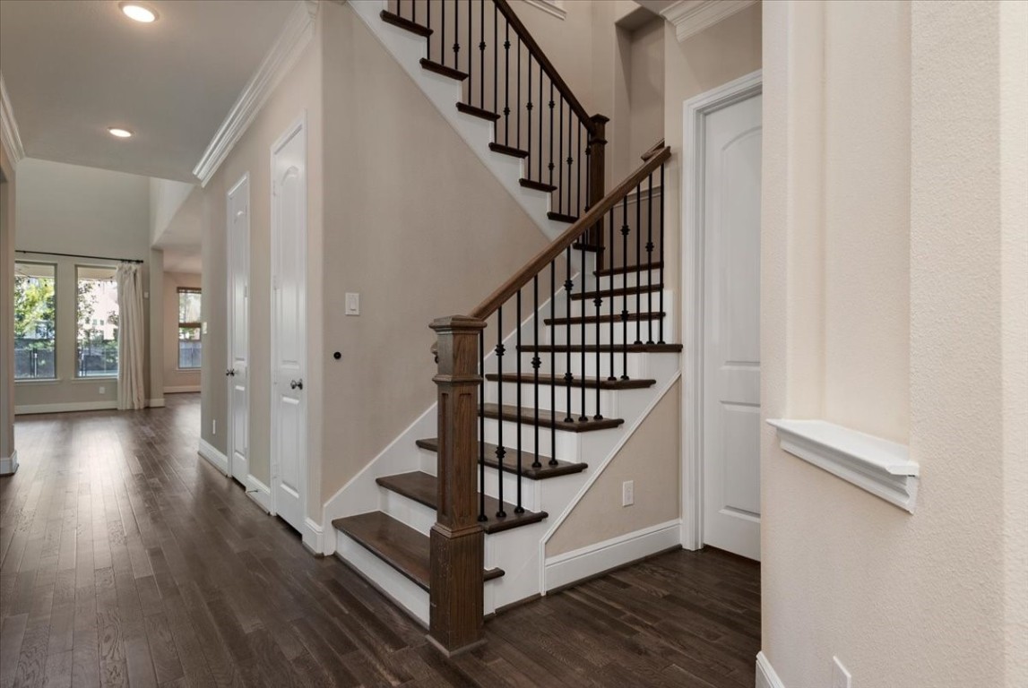 155 Rockwell Park Spring, TX 77389 - Photo 7 of 50 The photo showcases a bright, open entryway featuring a staircase with dark wood steps and elegant wrought iron railings. The space has hardwood floors and leads to a living area with large windows, offering ample natural light.