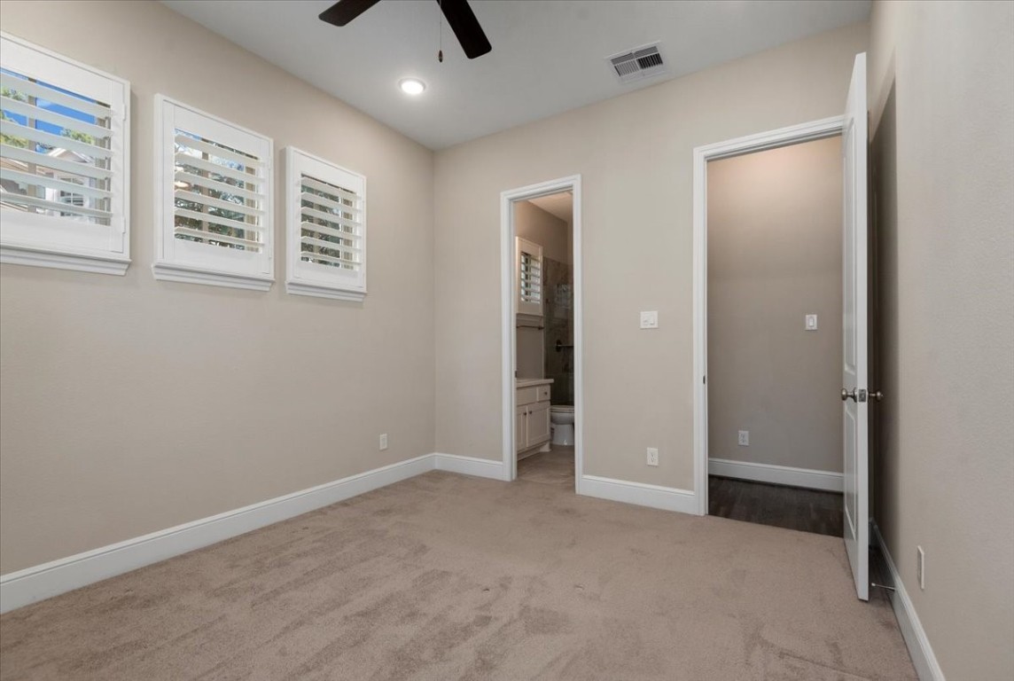 155 Rockwell Park Spring, TX 77389 - Photo 9 of 50 This photo shows a cozy bedroom with soft carpet flooring, neutral walls, and a ceiling fan. It features three windows with shutters and an en-suite bathroom.