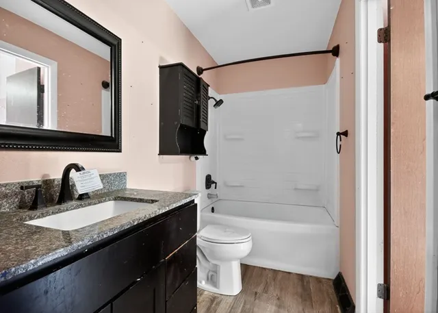 a bathroom with a granite countertop bathtub shower sink vanity mirror and toilet