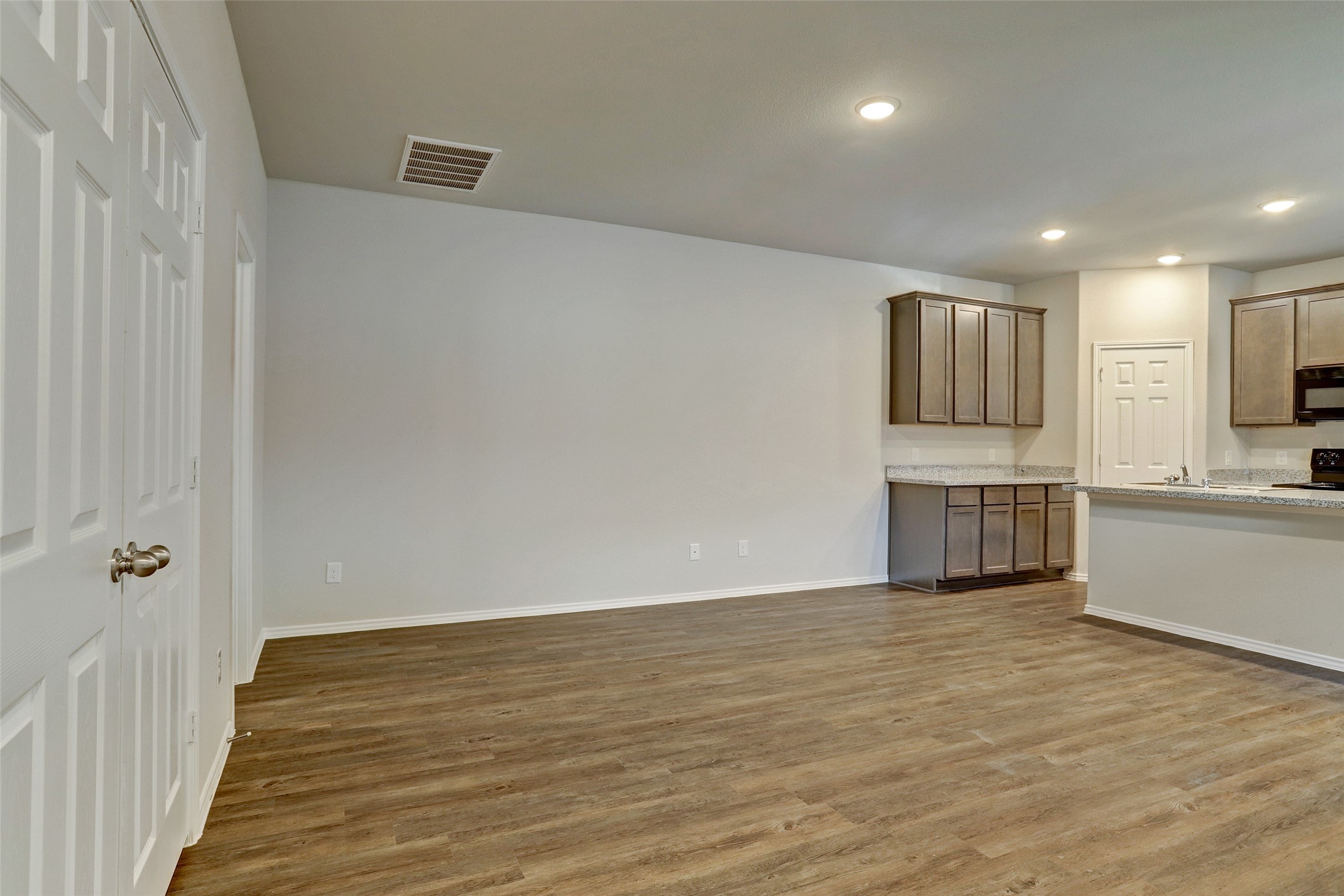 409 South 12th Street, Unit B Conroe, TX 77301 - Photo 3 of 14 This photo shows a spacious, open-concept living area with wood flooring and recessed lighting. It features a modern kitchen with granite countertops, ample cabinet space, and a nearby pantry or storage closet.