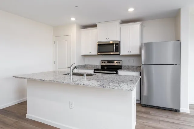 a kitchen with stainless steel appliances granite countertop a refrigerator a stove a sink a microwave a refrigerator and white cabinets with wooden floor