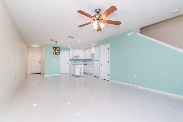 an empty room with a ceiling fan and a kitchen view