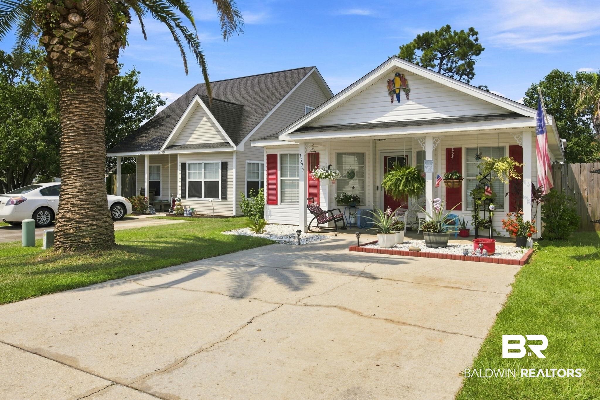 7577 Audubon Drive Foley, AL 36535 - Photo 5 of 33 Single-story residence featuring white siding and red shutters, a covered front porch with white columns, a concrete driveway, and a manicured lawn