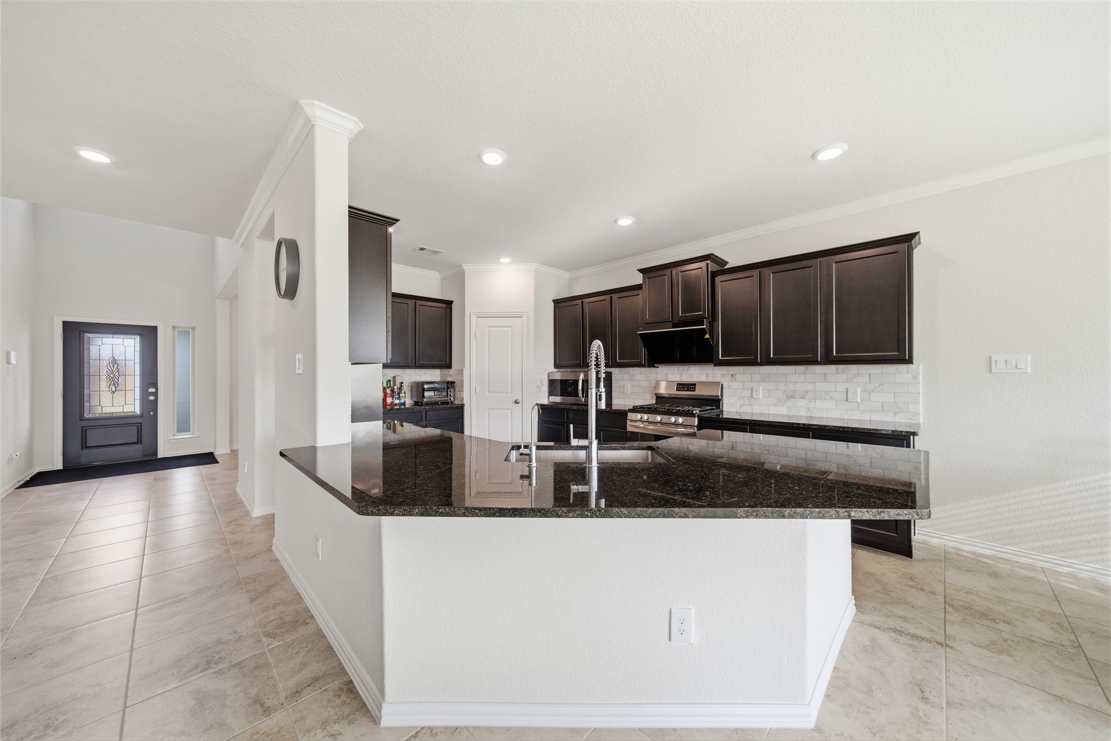 4335 Tawny Timber Drive Spring, TX 77386 - Photo 11 of 42 This bright kitchen features dark cabinetry, a large granite island with a modern sink, and stainless steel appliances. The open layout flows into a tile-floored entryway with a decorative front door, creating a welcoming atmosphere.