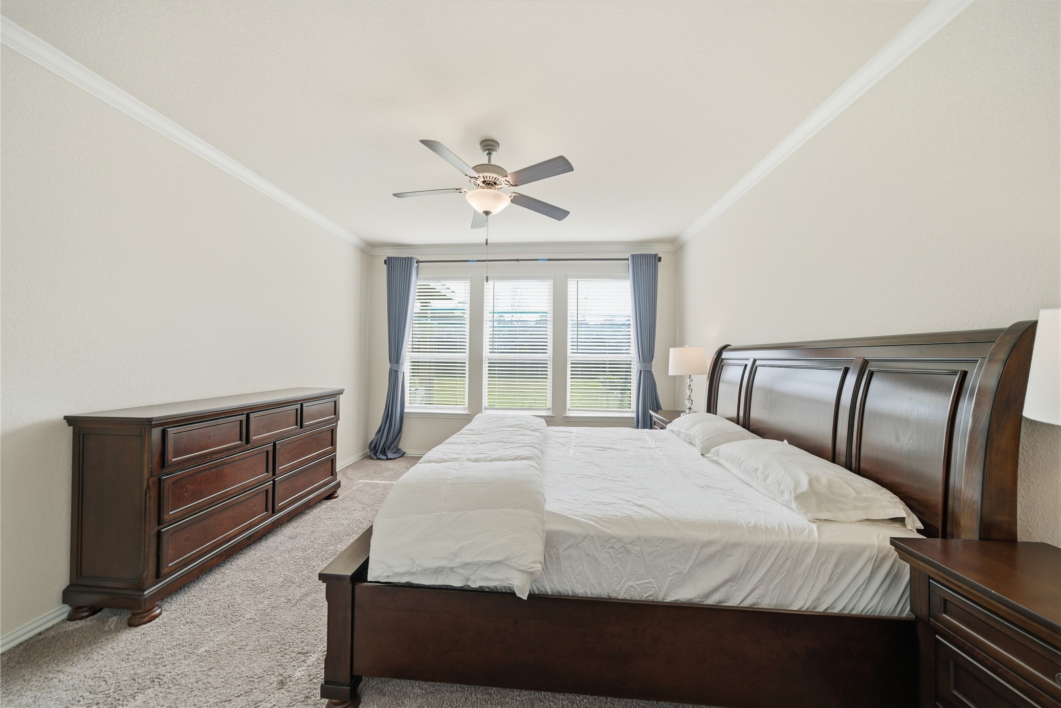 4335 Tawny Timber Drive Spring, TX 77386 - Photo 17 of 42 This spacious bedroom features a large bed, elegant wooden furniture, and ample natural light from wide windows with views. A ceiling fan adds comfort, while neutral walls create a serene atmosphere.